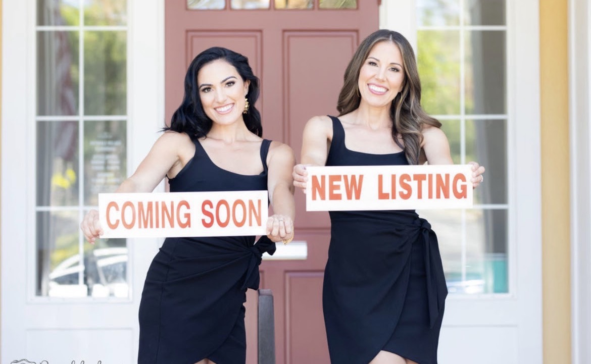 Julianna Sanchez and Cristina Nebot holding Coming Soon and New Listing signs in front of a red front door